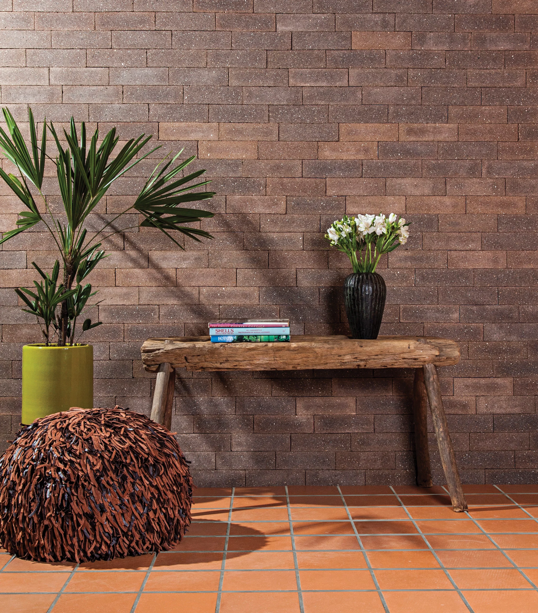 casa rústica com parede de tijolo aparente, vasos de planta e um banco de madeira com livros em cima